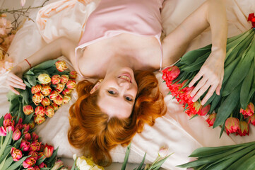 Young caucasian female relaxing with tulips and smiling in bed dressed in pink
