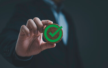 Businessman holding wooden round badge with green check mark symbol representing approval certification validation quality assurance success, business decision and verified acceptance.
