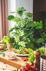 Delicious green salad with lettuce, strawberry, shrimps and nuts on oak table in bright cozy kitchen