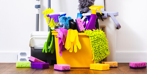 Cleaning products, household chemicals bottles and sprays, rags, sponges in orange bucket for...
