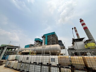 Obraz premium Industrial landscape showing a sprawling power plant with stacks, storage tanks, and containers against a blue sky representing energy production and industrial processes with environmental focus