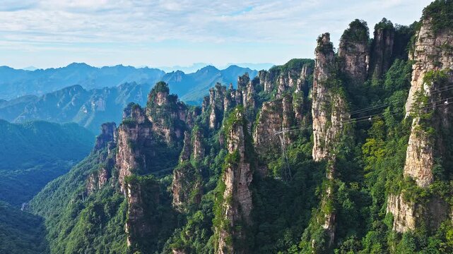 Aerial shot of the spectacular mountain landscape with unique rock pillars, lush green forest, and a cable car. Famous Zhangjiajie national forest park  in Hunan, China.