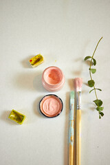 Creative flat lay of watercolor paints, brushes, and green branch on light background. Artistic workspace with pastel and vivid colors, perfect for design, craft, or creative inspiration