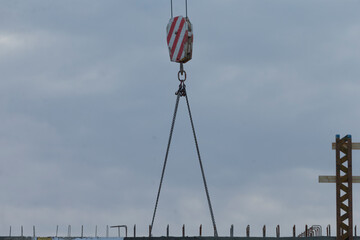 A crane hook suspended in mid-air at a construction site, set against a backdrop of cloudy skies,...