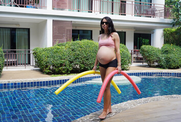 Pregnant young woman about to do exercises in pool with foam swim noodles