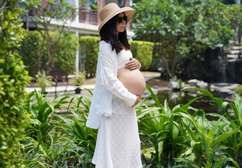 A pregnant woman with hat and sunglasses stands in the tropical garden