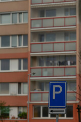 A clear blue parking sign stands in front of a multi-story residential building, showcasing urban...