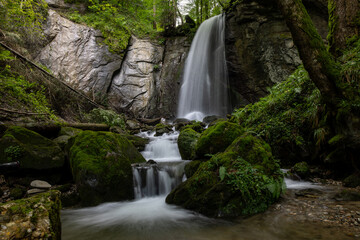long exposure of a scenic waterfall in a mossy green valley in Switzerland