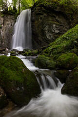long exposure of a scenic waterfall in a mossy green valley in Switzerland