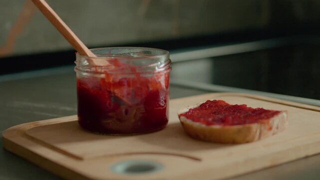 A delicious slice of bread generously spread with raspberry jam rests on a wooden chopping board in the kitchen, inviting a moment of simple pleasure.