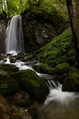 long exposure of a scenic waterfall in a mossy green valley in Switzerland