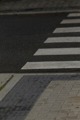 Obraz premium A close-up view of a pedestrian crosswalk featuring white stripes against dark pavement and textured tiles, highlighting urban infrastructure.