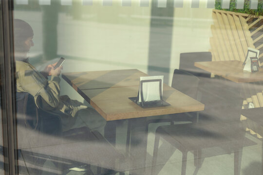 A person is casually sitting at a dining table within a bustling restaurant, focused intently on their smartphone device in front of them