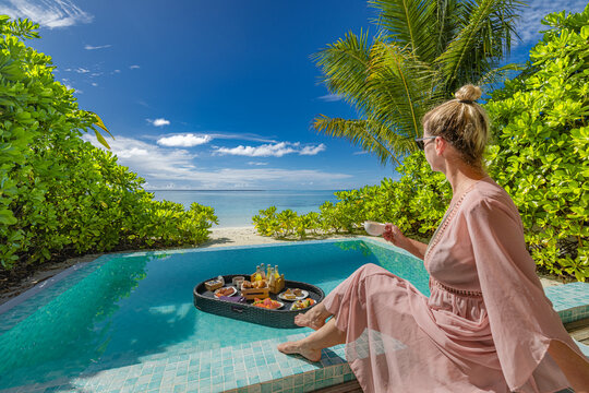 Sexy elegant woman relaxing poolside with cocktails on lounge chairs under umbrella, paradise island beach view, tropical resort luxury, floating breakfast on calm pool water for summer vacations - Powered by Adobe