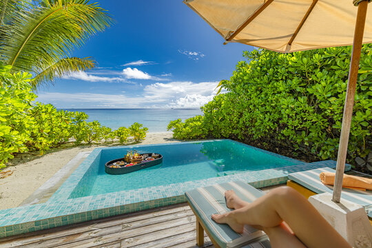 Sexy woman relaxing by the pool with legs on lounge chairs under umbrella, paradise island beach and ocean view, tropical resort luxury, floating breakfast on calm pool water for summer vacation and h