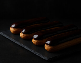 Four Chocolate Eclairs with Shiny Glaze on a Dark Background