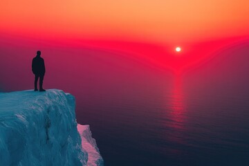 Silhouette of a person standing on a snow-covered cliff overlooking a vibrant red sunset over the ocean.