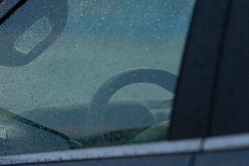 A close-up view of a steering wheel seen through a wet car window, capturing the essence of a rainy...