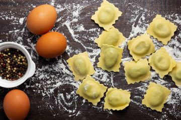 Fresh stuffed ravioli big size on wooden table with flour and eggs