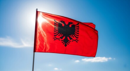 The national flag of Albania waving proudly in the wind against a bright blue sky with a brilliant sun flare