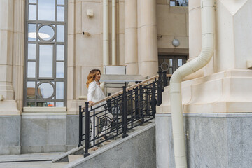 Woman White Building Stairs - A woman walks down the stairs of a white building with a large window.