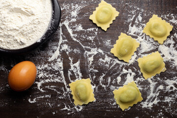 Fresh stuffed ravioli big size on wooden table with flour and eggs