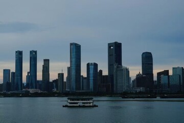 Naklejka premium Modern glass skyscrapers rising along the riverside, reflecting the water and city skyline.
