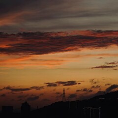 Fototapeta premium A dramatic sky filled with fiery burning clouds at sunset, with distant power towers standing tall against the horizon.