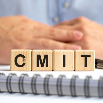 Wooden blocks spelling out the word CMIT on a white surface