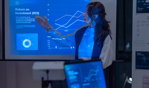 asian leader woman present  business presentation in a dimly lit office, analyzing financial charts and data projections on a screen