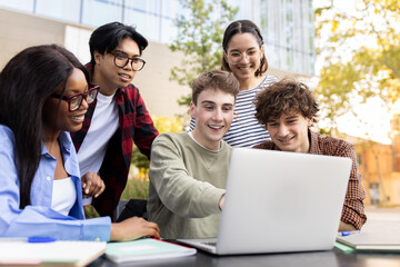 University students collaborating on a project using laptop outdoors