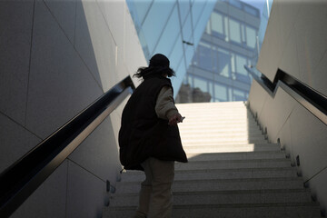 Fototapeta na wymiar A person is seen walking up a set of stairs while a tall building stands prominent in the background, creating an interesting contrast