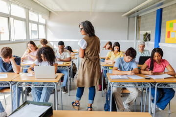 Group of diverse young students focused on completing their high school exam while teacher...