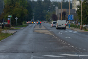 A serene view of an urban street on a rainy day, featuring cars and lush greenery, with wet pavement reflecting the sky.