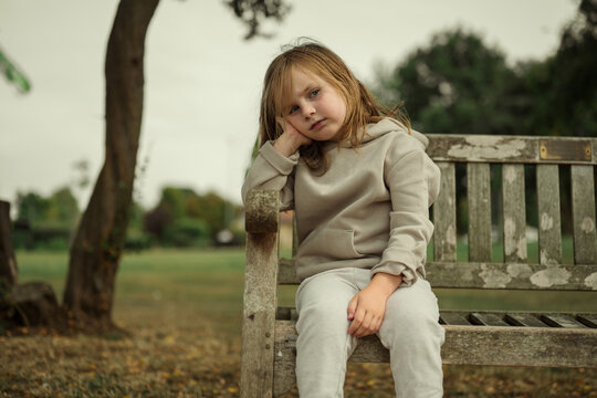 Bored, upset little girl sitting on a bench in the park