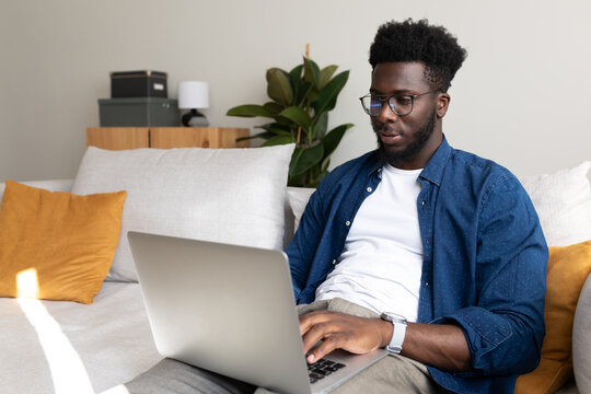 African American young man sitting on the sofa at home living room using laptop.
