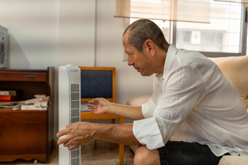Mature Latino man enjoys the refreshing cool air from a portable air conditioning unit in his...