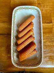 Traditional Middle Eastern tulumba pastries glazed with syrup, arranged on a patterned serving dish, ideal for dessert, Ramadan, and culinary backgrounds