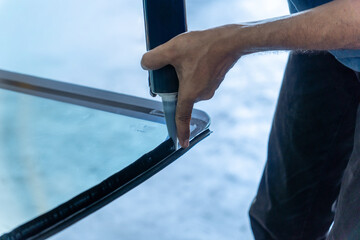 A close-up shot of an automotive glass repair technician's hands applying a glass sealant to a car's windshield. Car maintenance and repair concept.