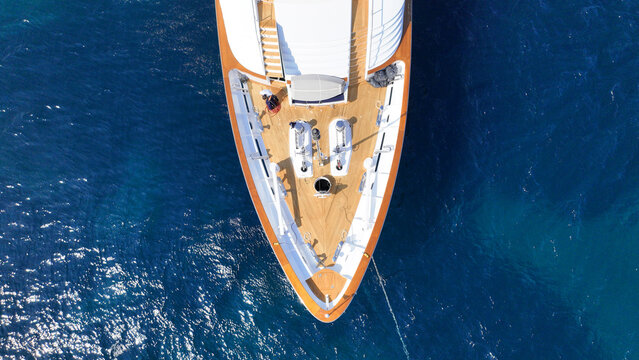 Aerial drone top down photo of luxury yacht with wooden deck anchored in deep blue Aegean sea, Mykonos island, Cyclades, Greece