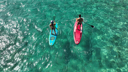 Aerial drone photo of unidentified fit couple practising SUP or Stand Up Paddle surf board in tropical mediterranean clear sea sandy beach
