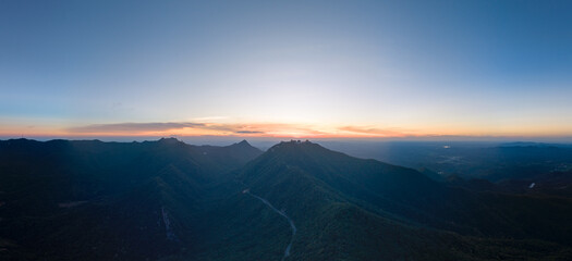 A vast panorama shows forested mountains at sunrise in Suizhou, China, with a warm glow on the...