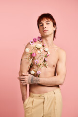 Handsome young man adorned with flowers poses elegantly against a soft pink background