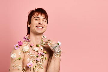 Elegant young man adorned with flowers exudes charm against a soft pink backdrop