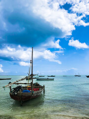 Fototapeta premium Fishing on wooden boats, catching fish with a net, working on the water in the ocean, Indian Ocean, Zanzibar. Old boat is floating in the ocean with a few other boats in the background. The sky is clo