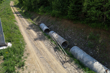 A dirt road winding through a forested slope highlights a path to a remote area. Pipes left along...