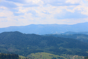 Obraz premium A layered mountain landscape where forested slopes give way to blue peaks in the distance. This image conveys the tranquility and majesty of nature, showing its boundlessness and beauty under a large 