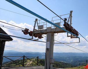 This photograph shows the top station of a cable car with a part of the mechanism that leads to a mountain ridge covered with forests. The image conveys technology that harmoniously fits into the wild