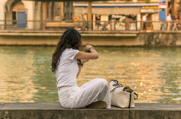 A young Chinese tourist wearing a white dress taking pictures of the Limmat river in Zurich at...