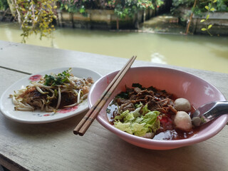 Spicy noodle soup with meat and vegetables by riverside, savory broth, chopstick resting on bowl,...